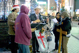十字架を携えて輪になってクリスマスソングを歌う有志たち＝２５日、東京・新宿駅東口のアルタ前で
