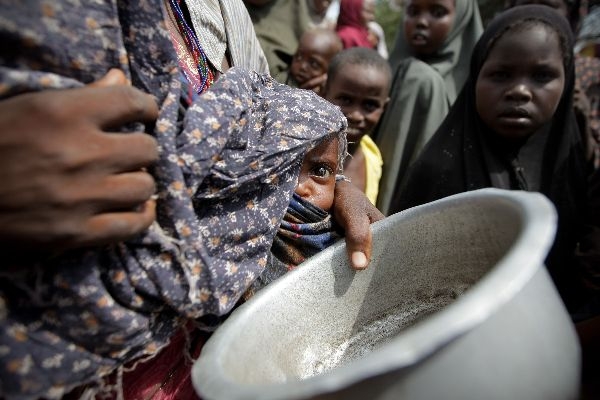 栄養失調の赤ちゃんを抱えながら食糧配給の列に並ぶ女性が配給を受ける器を手にしている。２０１１年７月２０日、ソマリア首都モガディシオで（写真提供=国際連合）。 