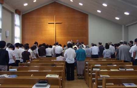 最後の集会で講壇の前に出て心をひとつにして祈る参加者たち＝８月３日、大阪市の岸之里キリスト教会で